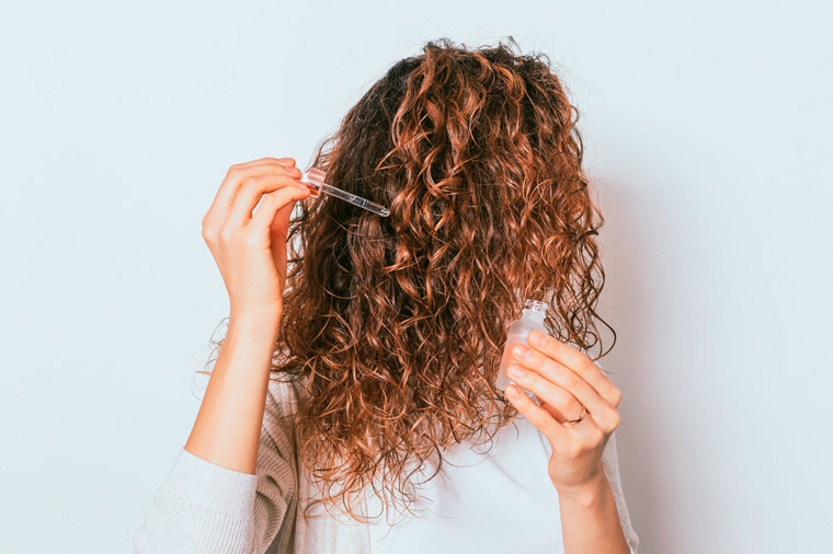 Mulher ruiva com cabelo cacheado aplicando óleo nos fios.